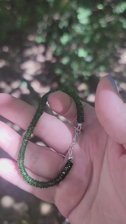 A person holding a green beaded bracelet in a hand in an outdoor environment
