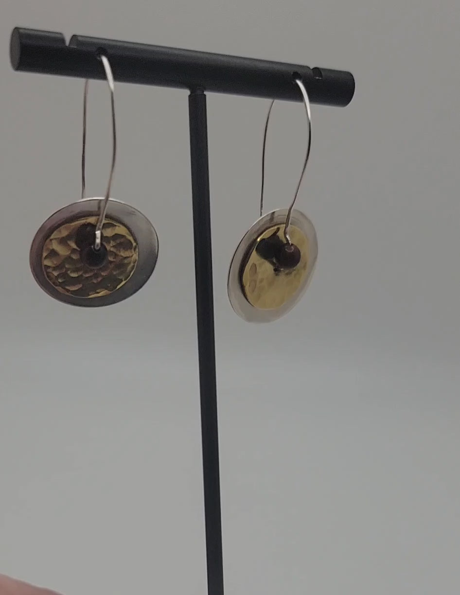 Pair of brass and silver earrings being rotated on a stand against a white background