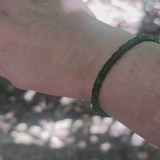 A person showing different angles of a green beaded bracelet being worn on a wrist in an outdoor environment