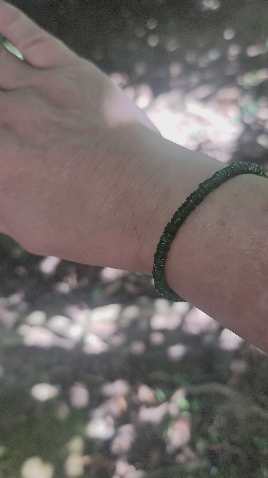 A person showing different angles of a green beaded bracelet being worn on a wrist in an outdoor environment
