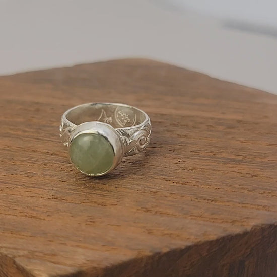 Round Aquamarine gemstone in sterling silver bezel setting with floral patterned band in white display block on a wood platform.