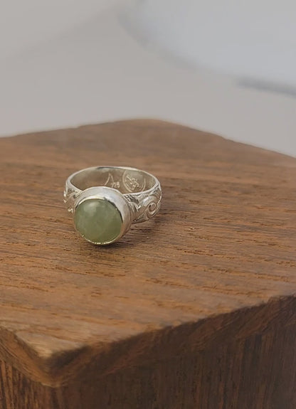 Round Aquamarine gemstone in sterling silver bezel setting with floral patterned band in white display block on a wood platform.