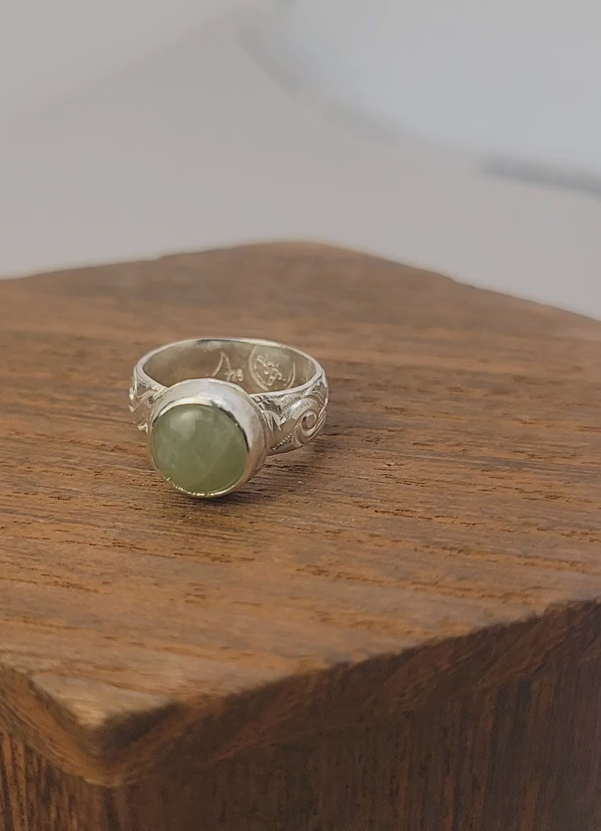 Round Aquamarine gemstone in sterling silver bezel setting with floral patterned band in white display block on a wood platform.
