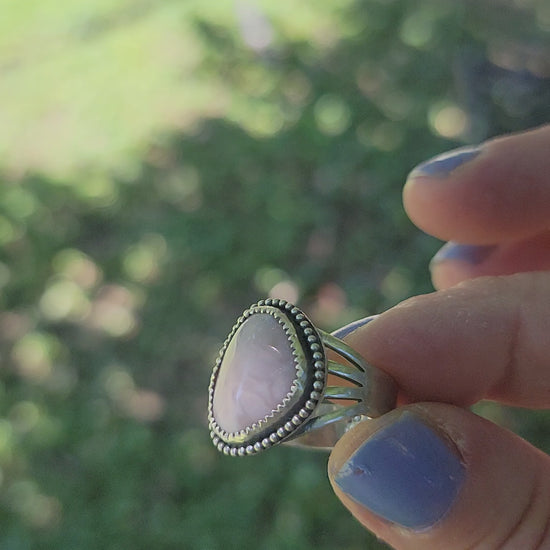Pink gemstone ring shown in hand in natural outdoor environment