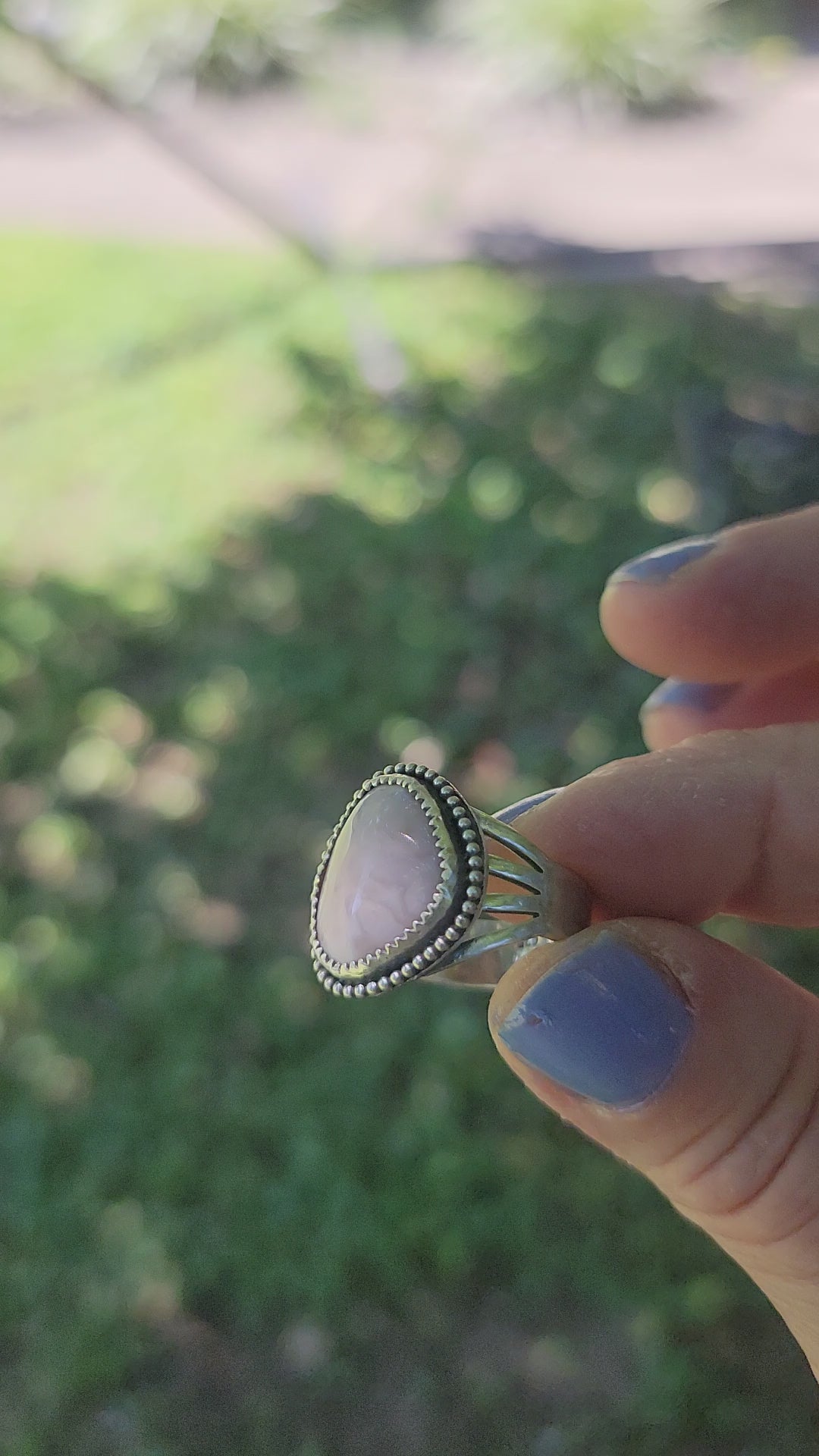 Pink gemstone ring shown in hand in natural outdoor environment