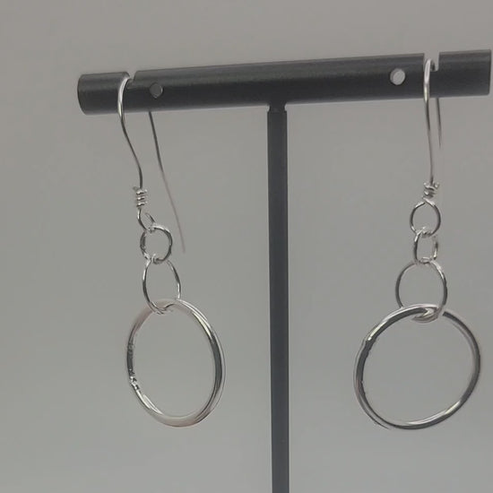 Silver earrings on a black earring stand on a gray background