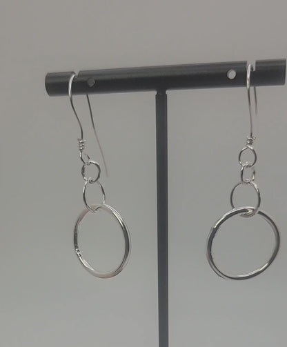 Silver earrings on a black earring stand on a gray background