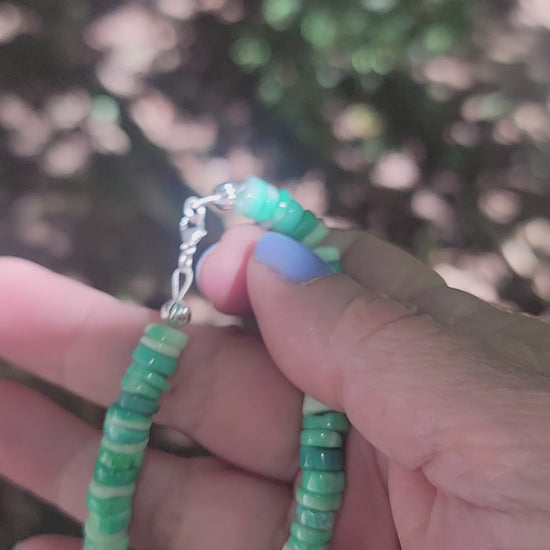 Peruvian opal beaded bracelet finished with a sterling silver lobster clasp being held by a hand in an outdoor environment.