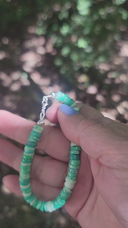 Peruvian opal beaded bracelet finished with a sterling silver lobster clasp being held by a hand in an outdoor environment.