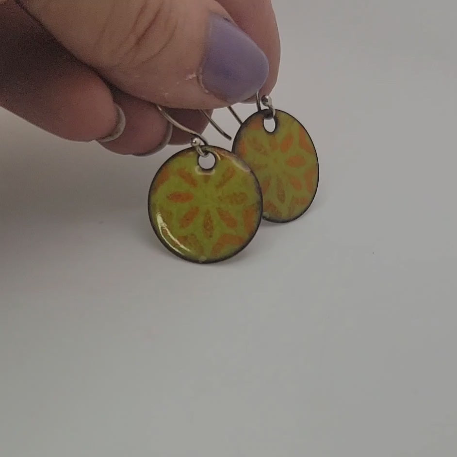 Hand holding a pair of green and orange earrings on a white background