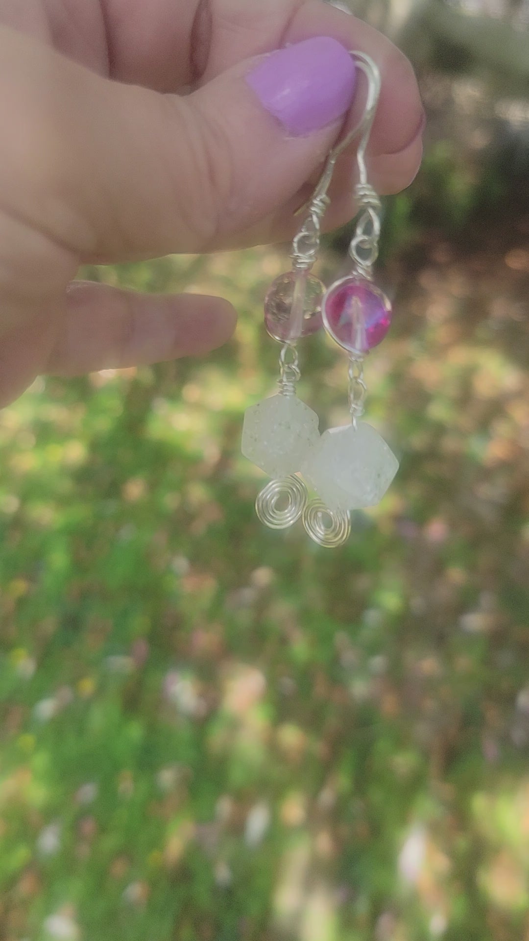 Hand holding a pair of pink and crystal dangle earrings with silver wire wrap and ear wires