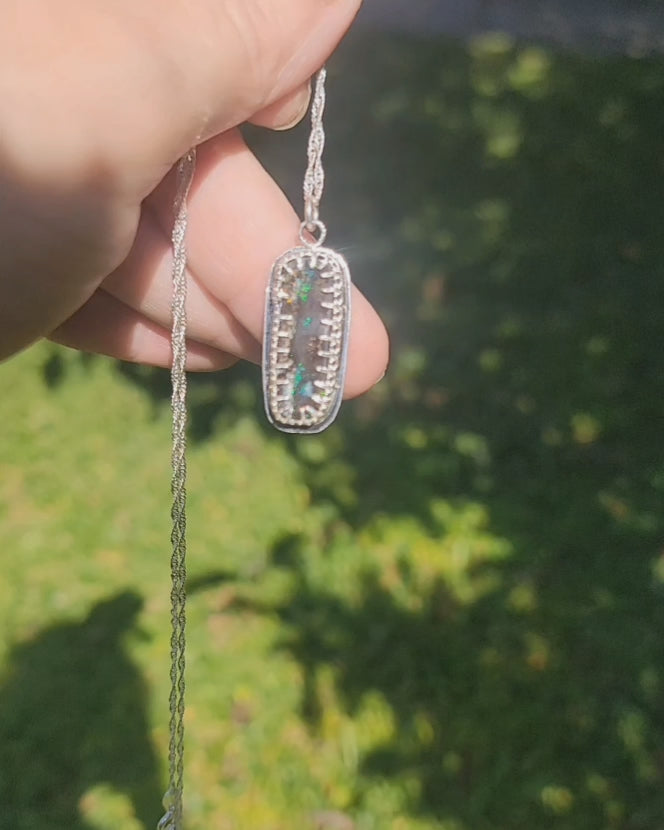 Video of bezel set iridescent stone with flashes of green and teal being held by and in natural outdoor environment