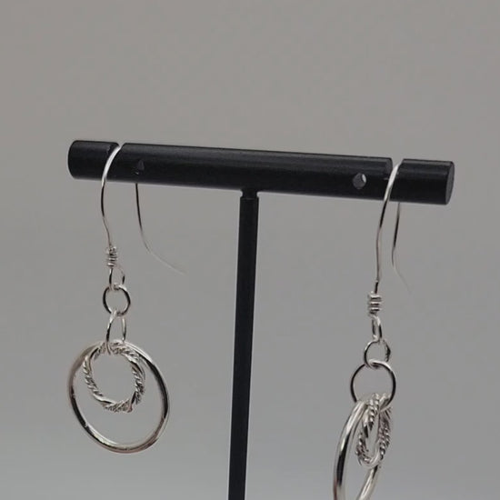 Silver double hoop earrings on black earring stand on gray background
