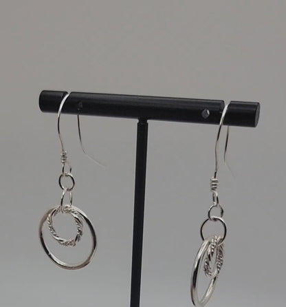 Silver double hoop earrings on black earring stand on gray background