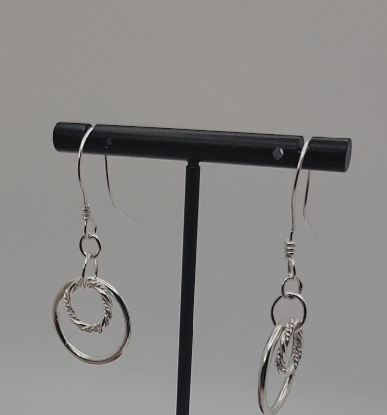 Silver double hoop earrings on black earring stand on gray background