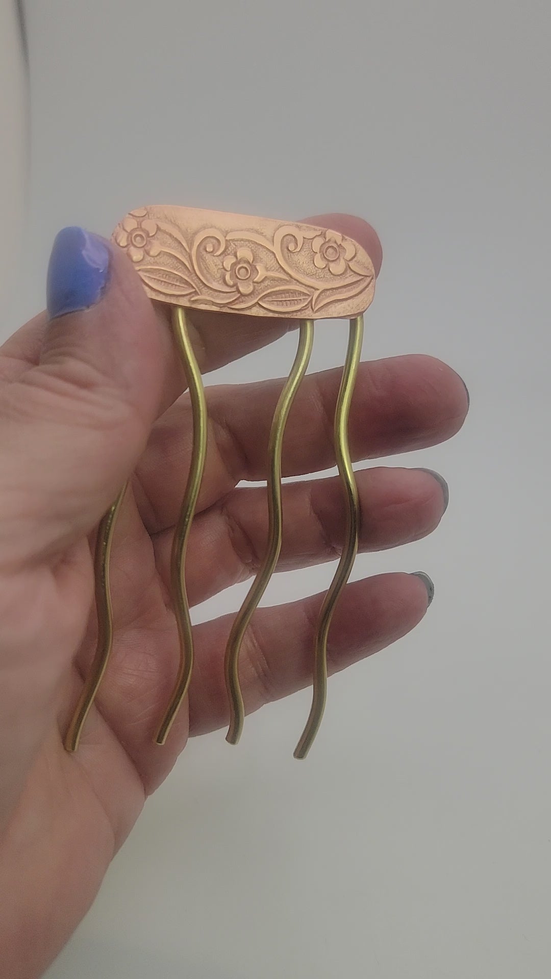 Hand holding a brass and copper hair fork against a white background