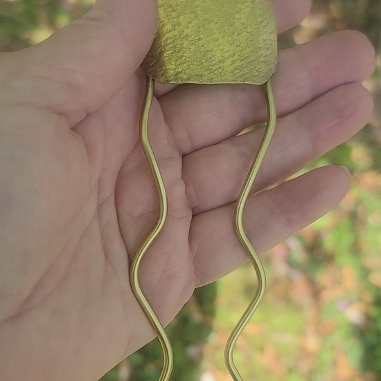 Hand holding a brass pin against nature background