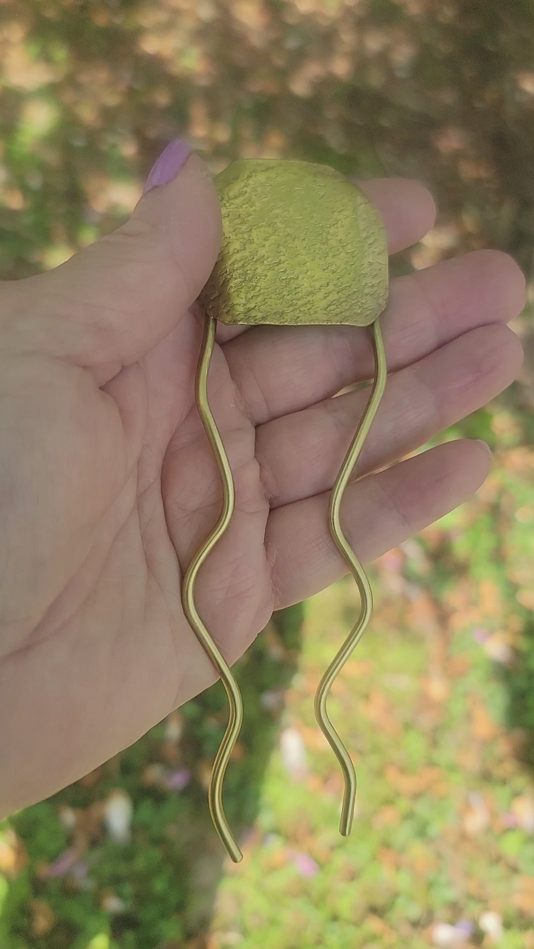Hand holding a brass pin against nature background