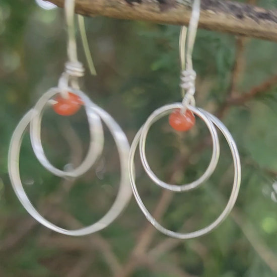 Handcrafted sterling silver hoop earrings with small orange-red carnelian beads in outdoor environment