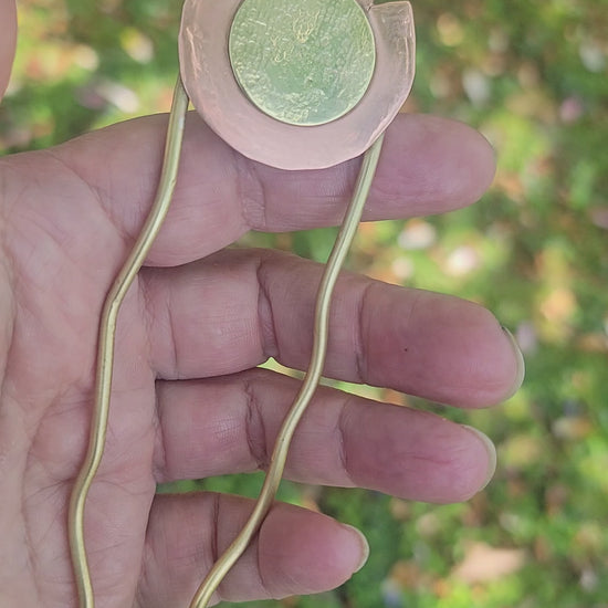 Hand holding a brass and copper hair pin on a nature background