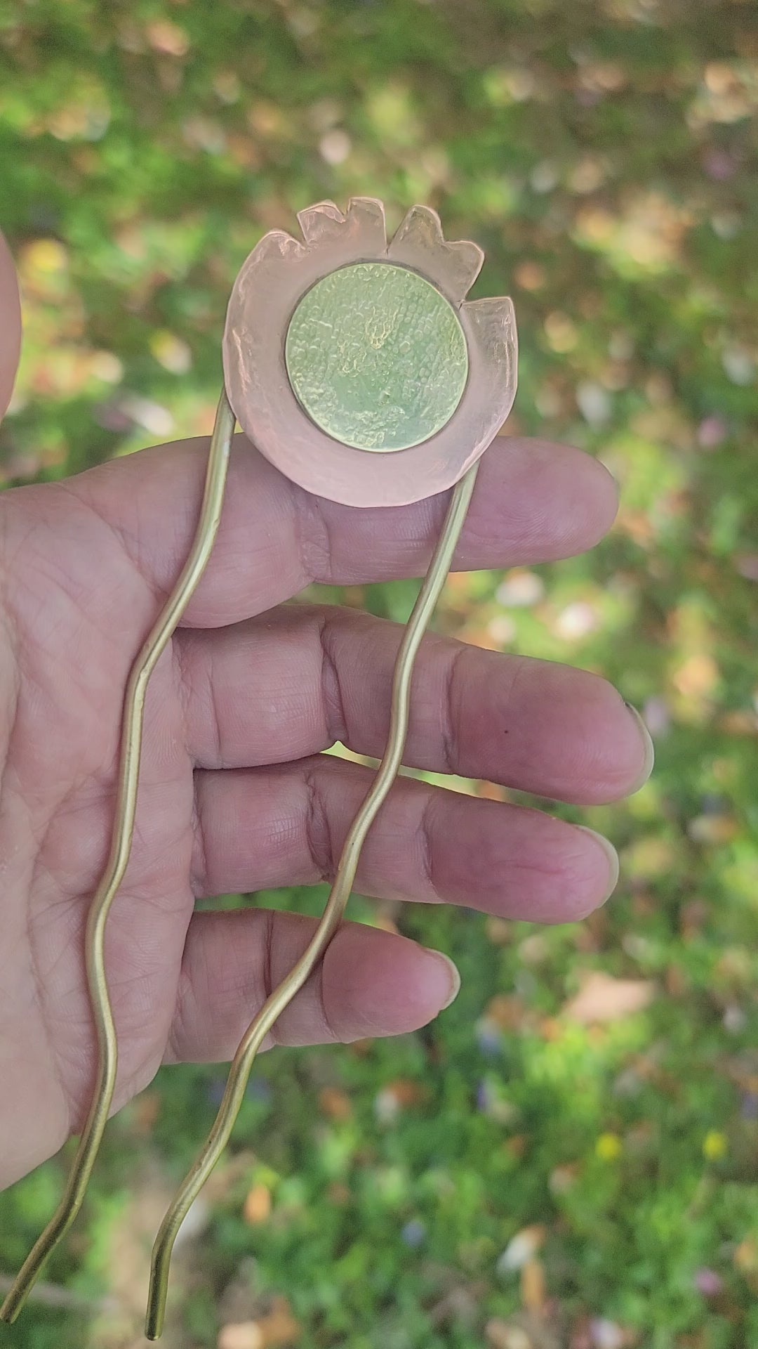 Hand holding a brass and copper hair pin on a nature background