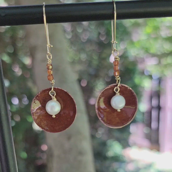 Round Dangle Copper earrings with pearl in center and orange beads on natural background