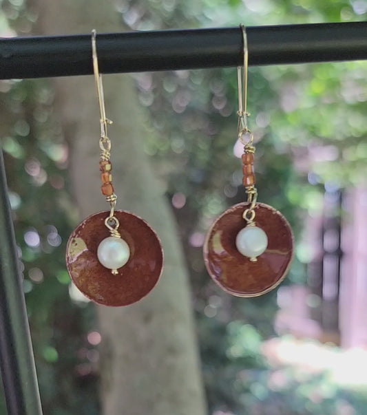 Round Dangle Copper earrings with pearl in center and orange beads on natural background