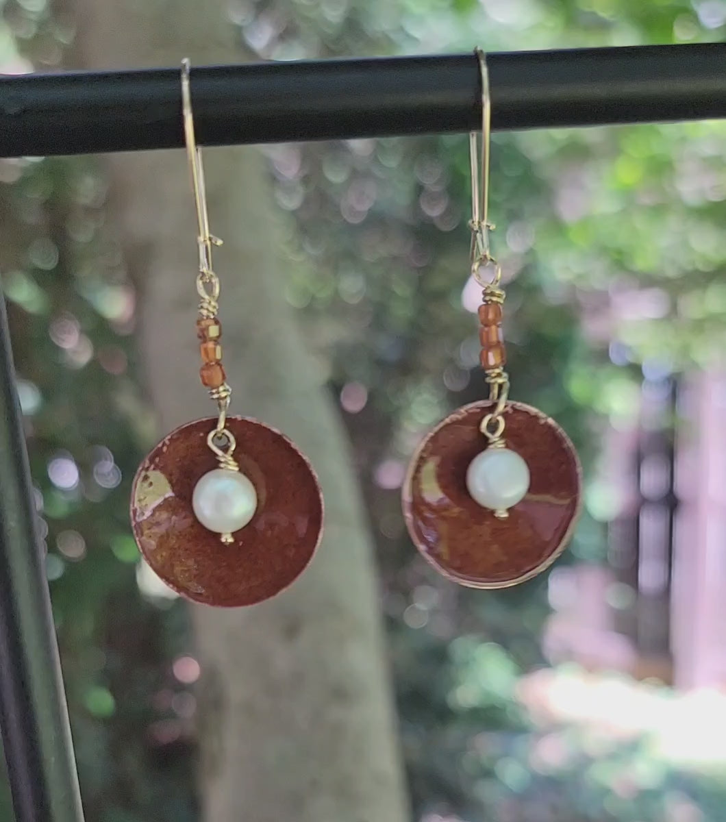 Round Dangle Copper earrings with pearl in center and orange beads on natural background