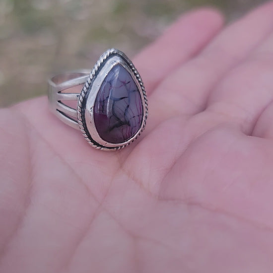 Hand holding a purple stone and silver ring outdoors