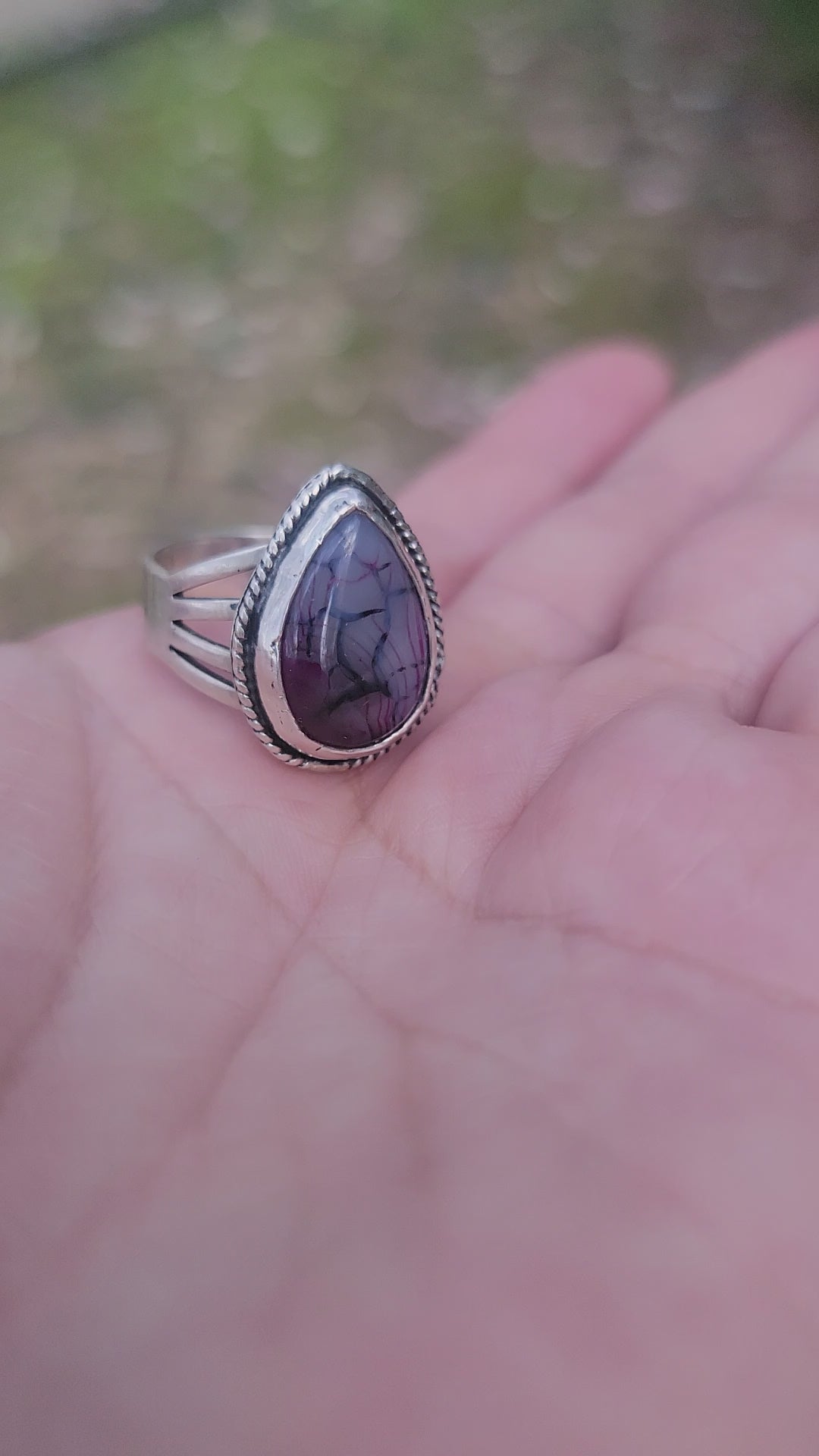 Hand holding a purple stone and silver ring outdoors