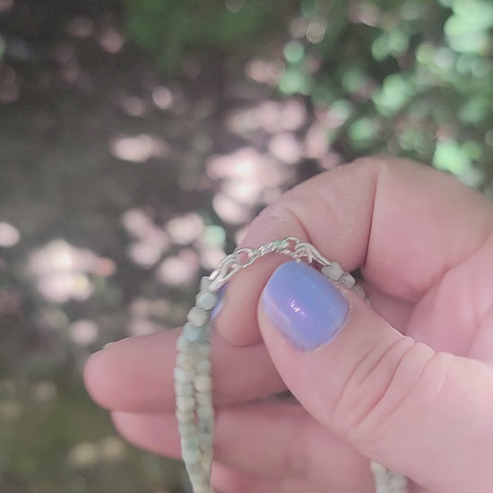 A Lemurian Blue calcite beaded bracelet with sterling silver lobster clasp being held in a hand in an outdoor environment.