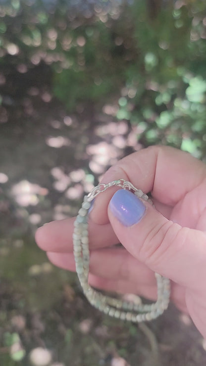 A Lemurian Blue calcite beaded bracelet with sterling silver lobster clasp being held in a hand in an outdoor environment.