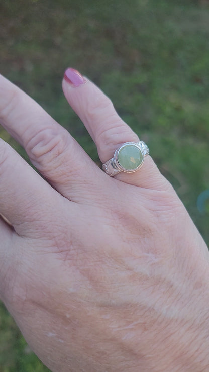 Round Aquamarine gemstone in sterling silver bezel setting with floral patterned band being shown worn on a hand in outdoor environment.
