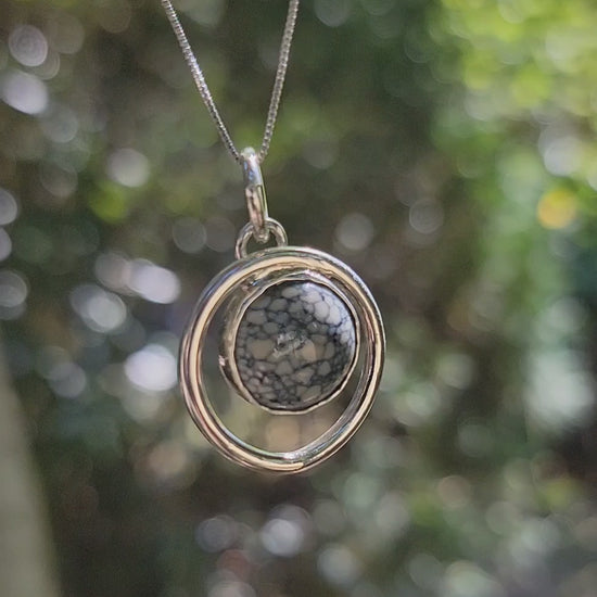 Handmade variscite pendant within an open sterling silver circle with movement in an outdoor environment