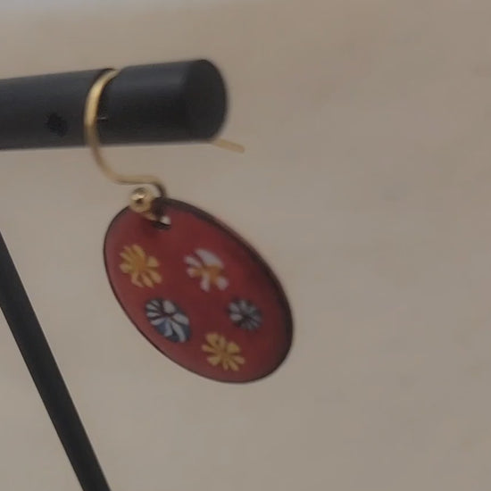 Video of red and floral enameled earrings dangling from black earring stand on beige background
