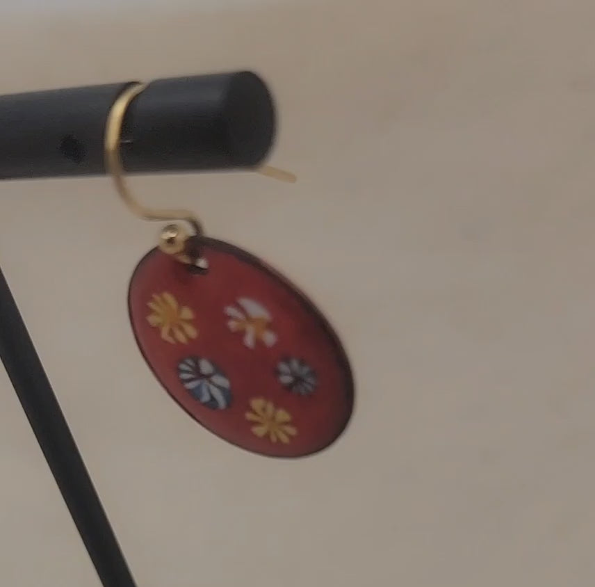 Video of red and floral enameled earrings dangling from black earring stand on beige background