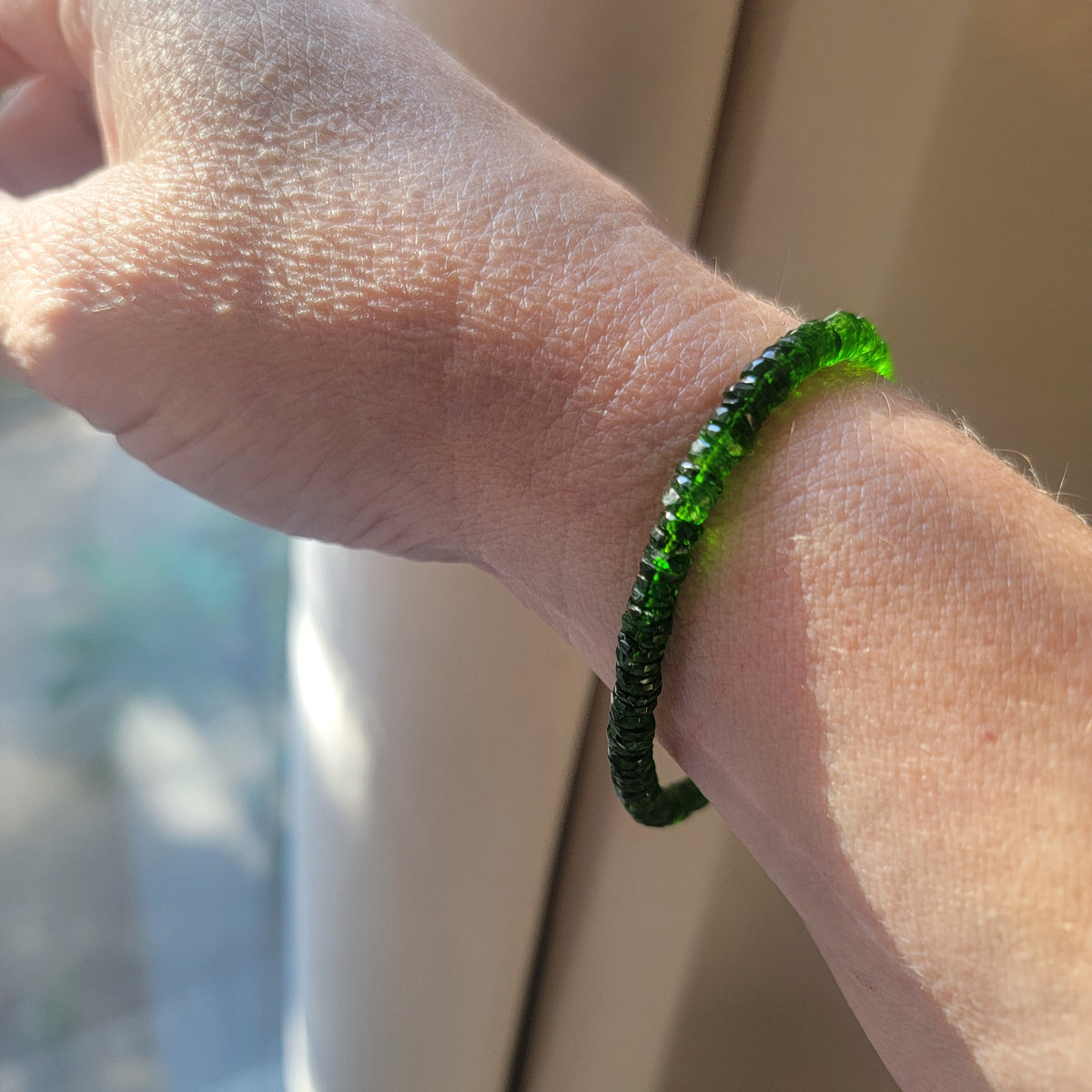 A green beaded bracelet worn on a hand next to a window