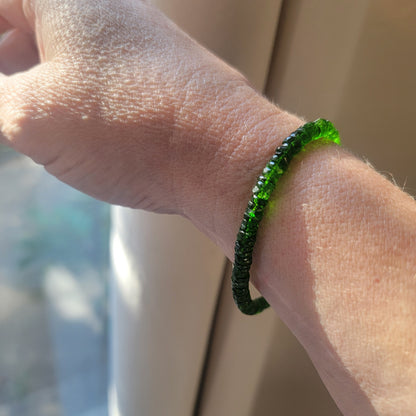 A green beaded bracelet worn on a hand next to a window