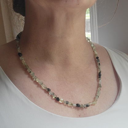 Green and black gemstone necklace being worn by a person next to a window
