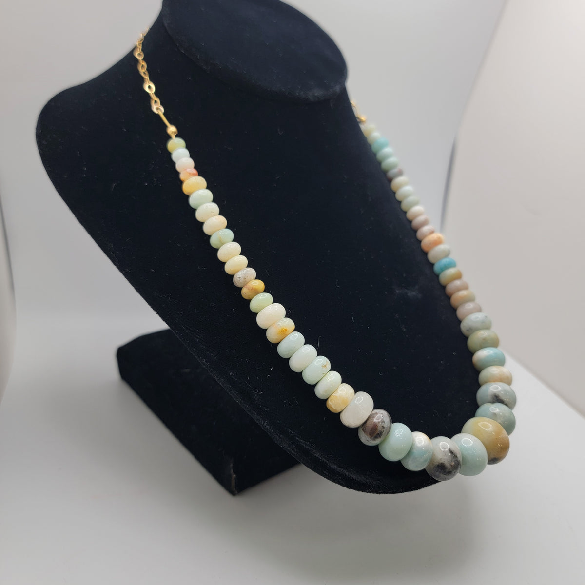 Blue and earthtone necklace on a black necklace bust on a white background