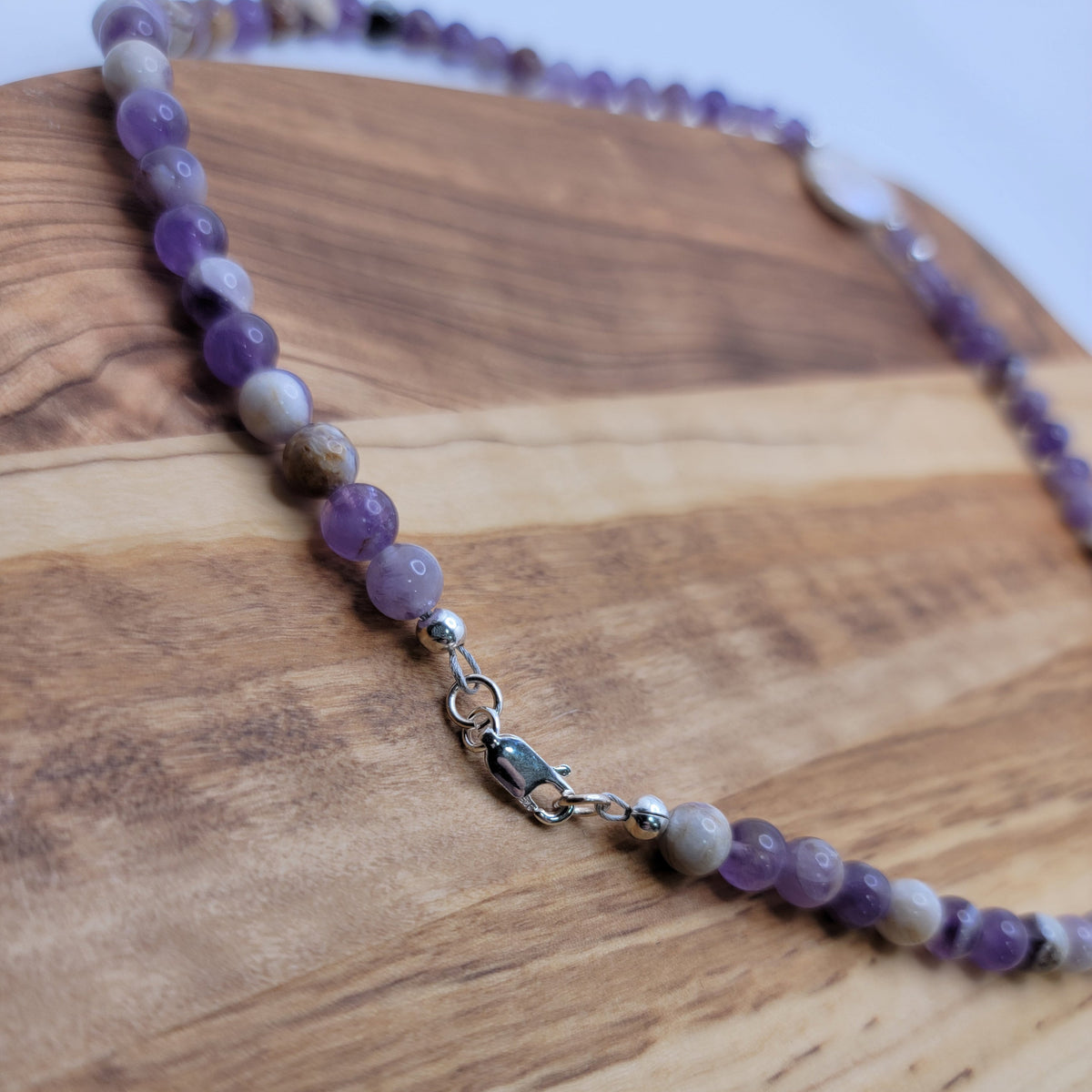 Amethyst and coin pearl necklace with a sterling silver lobster clasp on a wood platform on a white background