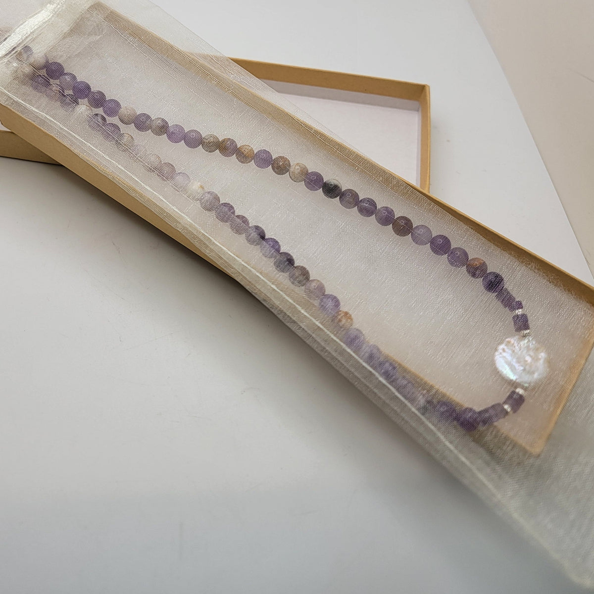 Amethyst and coin pearl necklace in an organza pouch in a cardboard gift box on a white background