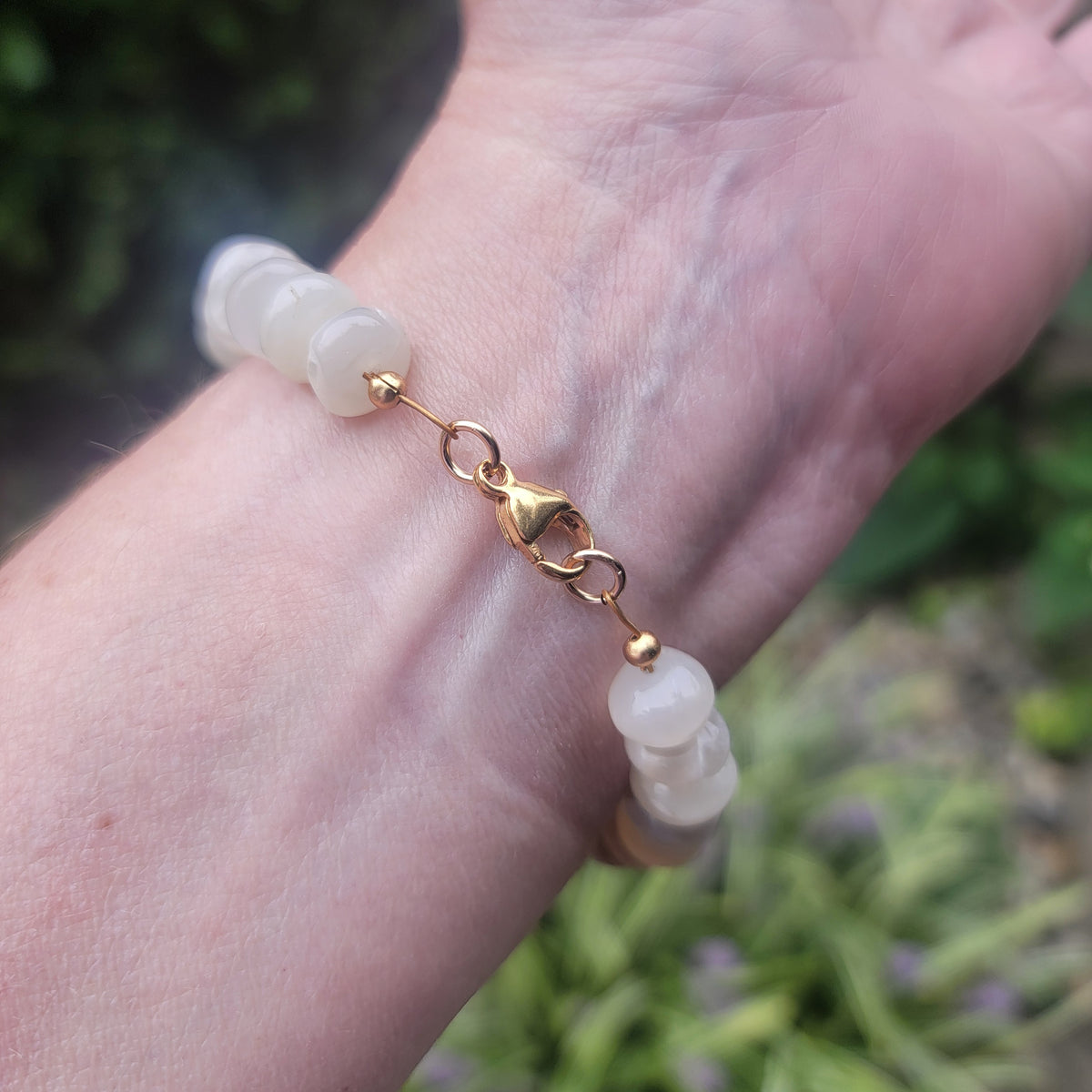 Moonstone beaded bracelet with gold colored lobster clasp being worn on wrist in natural outdoor environment