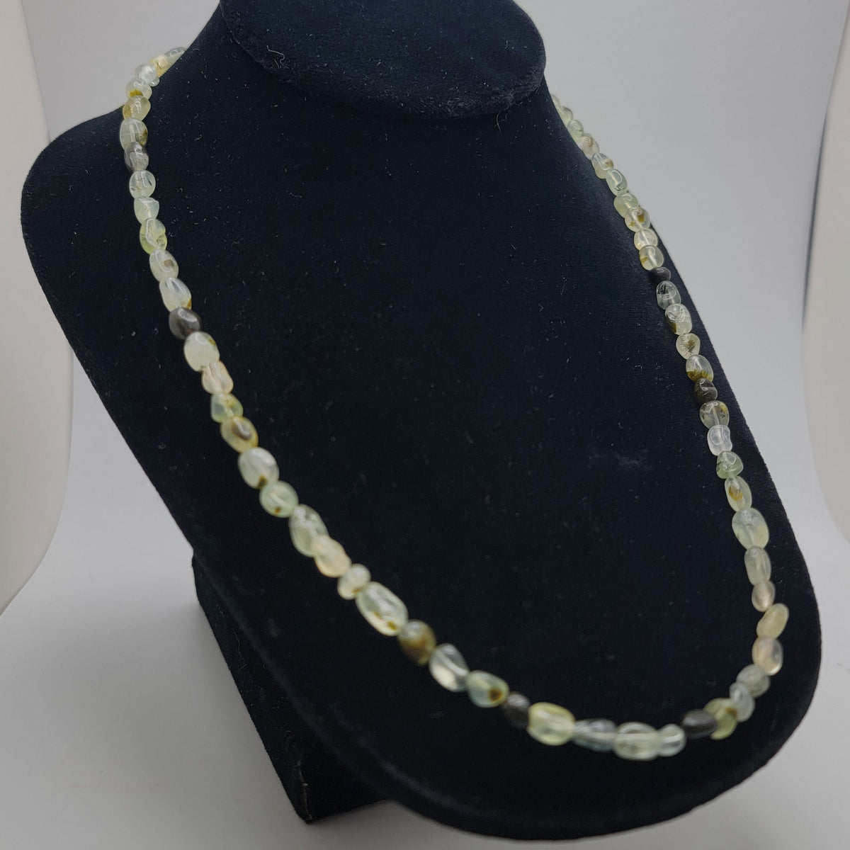 Green and black gemstone beaded necklace shown on black necklace bust on white background