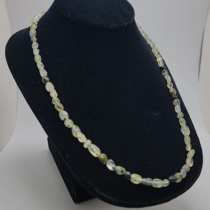 Green and black gemstone beaded necklace shown on black necklace bust on white background