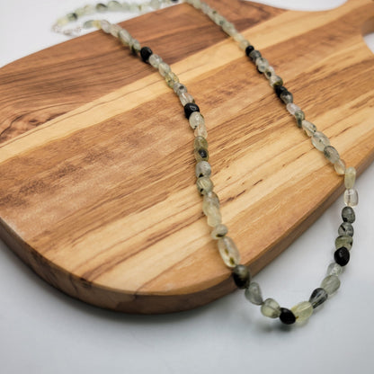 Green and black beaded necklace on a wood board on a white background