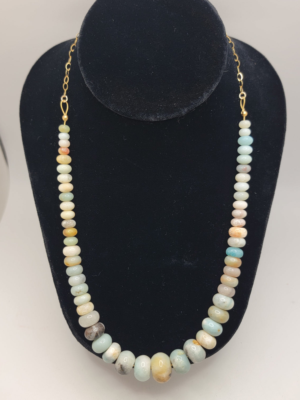 Blue and earthtone gemstone bead necklace with gold chain on a black necklace bust on a white background
