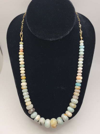 Blue and earthtone gemstone bead necklace with gold chain on a black necklace bust on a white background