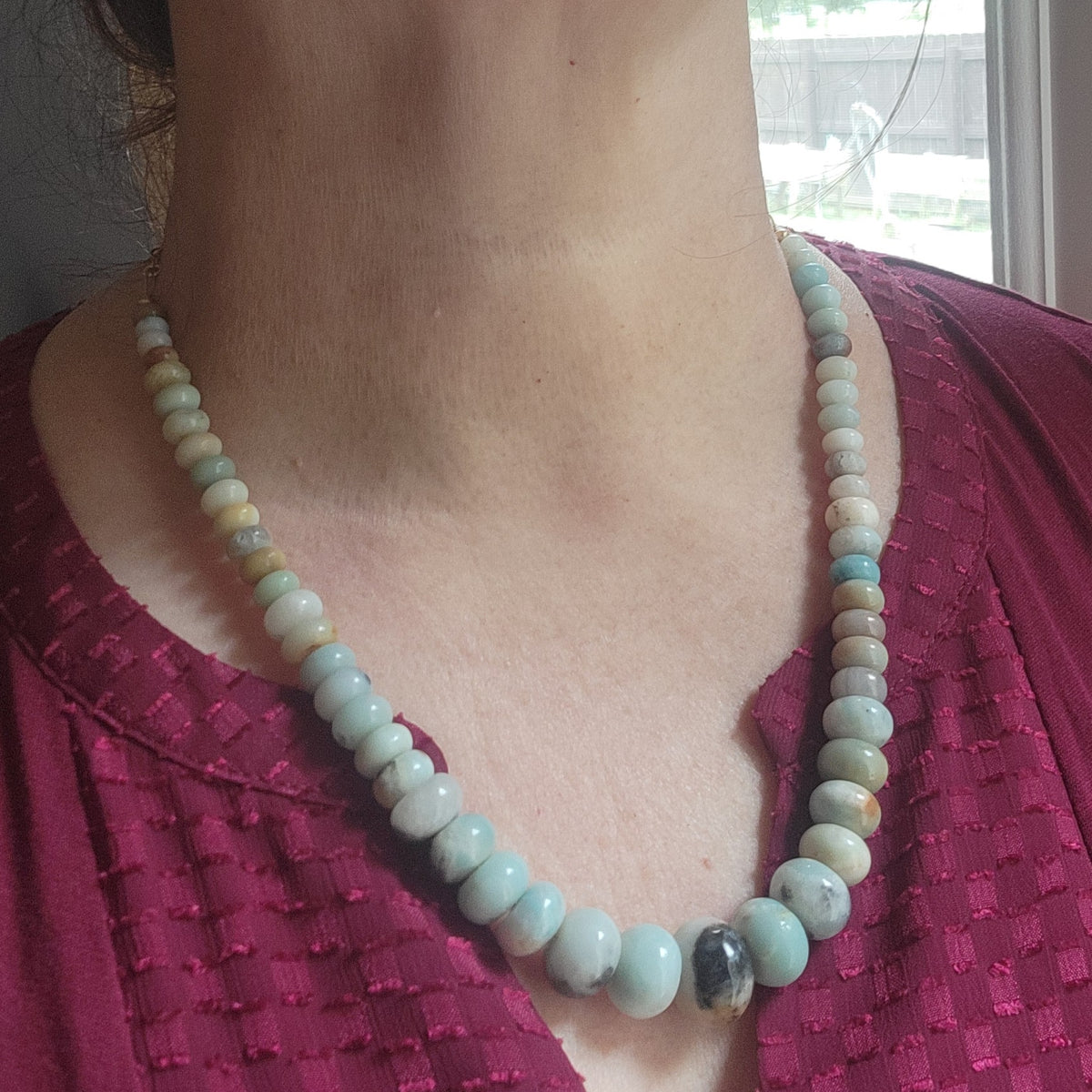 Blue beaded gemstone necklace being worn on a person next to a window