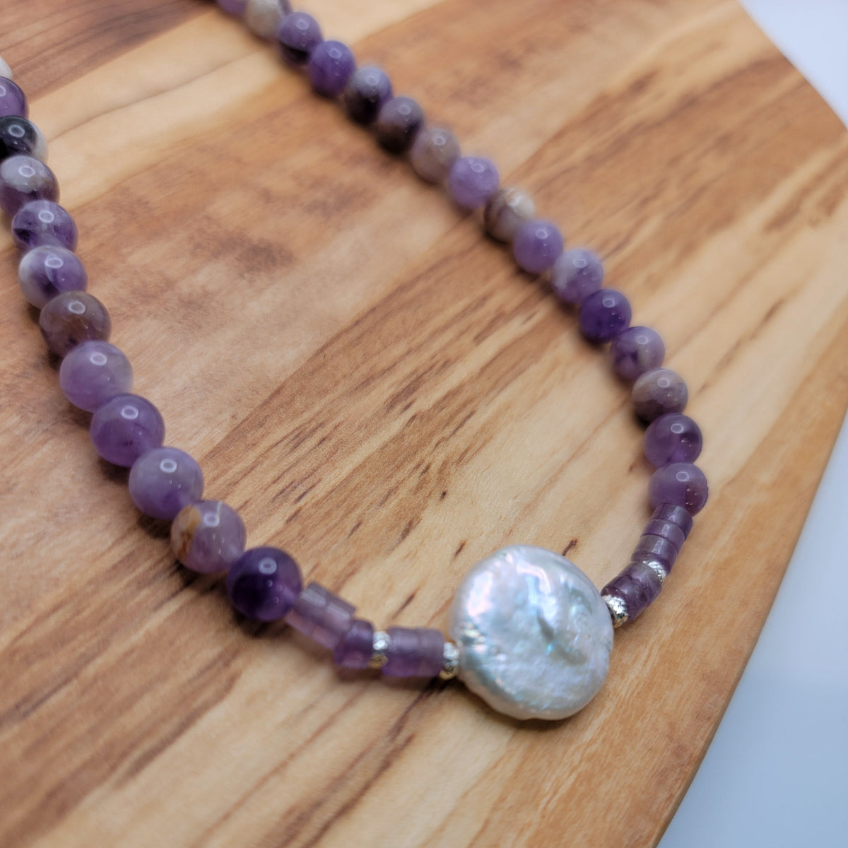 Amethyst and coin pearl necklace on a wood platform on a white background